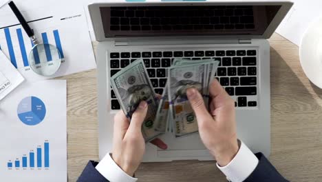 Entrepreneur-counting-dollar-bills-in-his-hands,-putting-them-on-laptop,-income