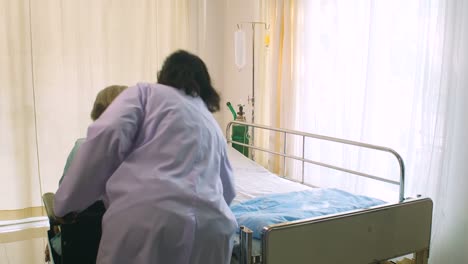 Professional-female-doctor-helping-her-patient-from-wheelchair-to-the-bed-in-hospital