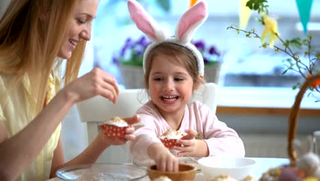 Joven-madre-y-su-pequeña-hija-con-orejas-de-conejo-divertidos-cocinar-cupcakes-de-Pascua