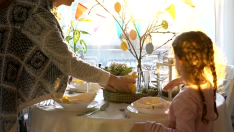 Woman-and-her-little-daughter-are-setting-easter-festive-table-with-bunny-and-eggs-decoration