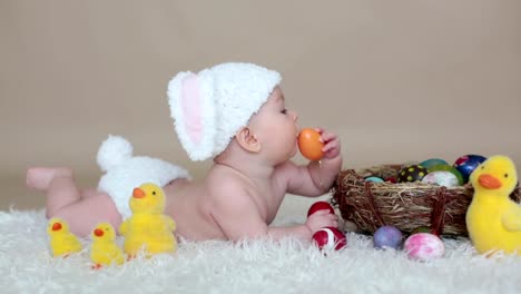 Cute-little-toddler-baby-boy,-playing-with-colorful-easter-eggs-and-little-decorative-ducks,-isolated-shot,-beige-background