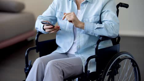 Female-pensioner-in-wheelchair-browsing-internet-on-smartphone,-communication