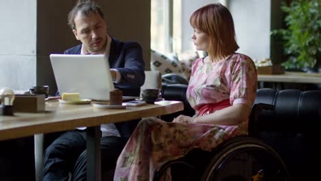 Woman-in-Wheelchair-and-Man-with-Laptop-Chatting-in-Cafe