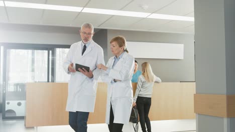 En-el-Hospital,-los-médicos-ocupados-hablan,-utilizando-Tablet-PC-mientras-camina-por-el-edificio.-En-el-paciente-antecedentes-habla-con-la-recepcionista.-Nuevo-centro-médico-totalmente-funcional-moderna.