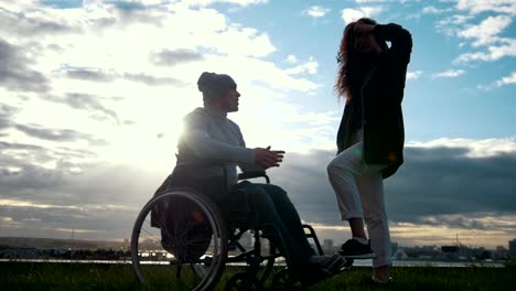 Disabled-man-in-a-wheelchair-with-woman-talking-at-the-cloudy-sunset