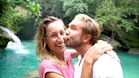 Young-couple-taking-selfie-portrait-with-a-beautiful-waterfall