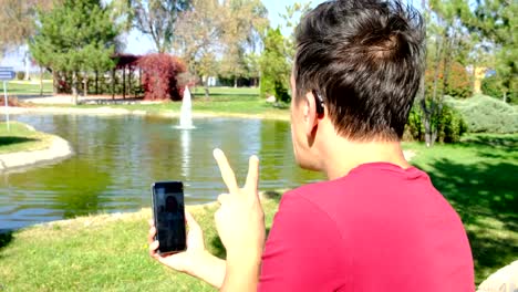 Young-deaf-boy-communicating-with-sign-language--at-smart-phone-in-park