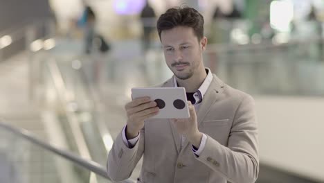 Handsome-young-businessman-writing-texts-on-digital-tablet-in-public-space