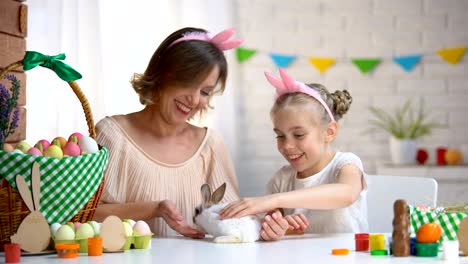 Madre-e-hija-admirando-conejito-esponjoso-blanco,-acariciando-y-jugando-con-él