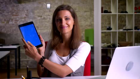 Attractive-female-office-worker-taps-twice-on-the-screen-of-tablet-smiles-and-shows-the-image-to-a-camera