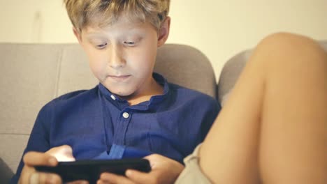 Boy-sitting-on-couch-holding-smartphone-in-hands-playing-game