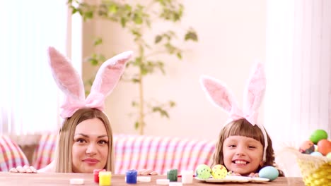 mother-and-daughter-in-rabbit-ears-look-out-from-under-the-table-and-look-at-each-other.