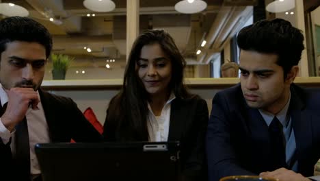 Handheld-shot-of-Indian-coworkers-colleagues-huddled-together-at-cafe-table-as-they-stare-at-a-laptop-screen-looking-concerned-and-thinking-for-out-of-box-solution-to-their-problems