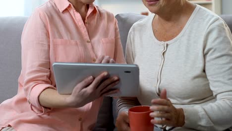 Hija-adulta-enseñando-a-mamá-vieja-a-usar-la-tableta,-mostrando-la-aplicación-de-videollamada