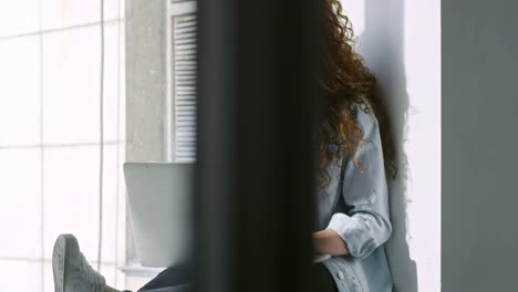 Mujer-joven-sentada-en-la-ventana-de-alféizar-y-escribiendo-en-el-ordenador-portátil