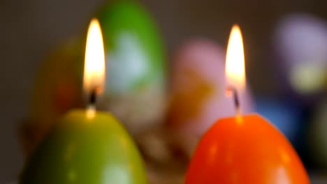 Candles-made-in-shape-of-easter-egg.-Green,-orange,-yellow.-Easter-eggs-candles-and-colorful-Easter-eggs-in-the-background.-Focus-and-refocusing.