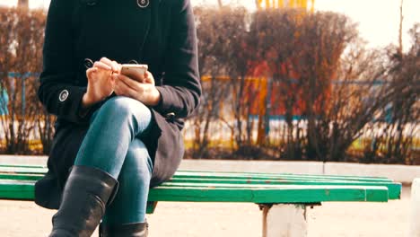 Junge-Frau-mit-Smartphone-auf-einer-Bank-im-Stadtpark