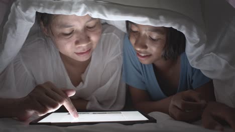 Asiatische-Familie-mit-Mutter-und-Tochter-Beobachten-die-Tablette-in-einer-Decke-auf-dem-Bett-zu-Hause