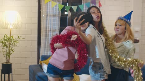 Group-of-Asian-women-party-at-home,-female-using-mobile-phone-making-vlog-selfie-to-social-media-while-funny-dance-together-in-living-room-in-night.-Young-friend-celebrate-holiday-concept.-Slow-motion