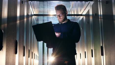 IT-support-engineer-in-glasses-is-operating-a-laptop-in-a-server-room