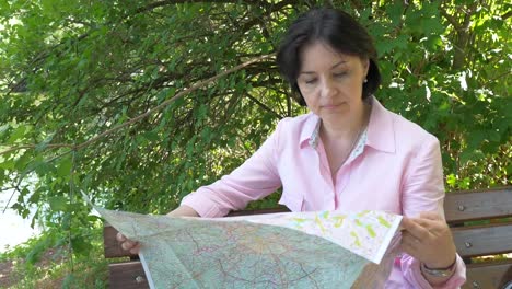 Brunette-looks-at-a-paper-map-in-the-park-near-the-pond