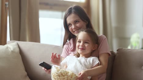 Mother-holding-remote-control-watching-tv-with-small-kid-daughter