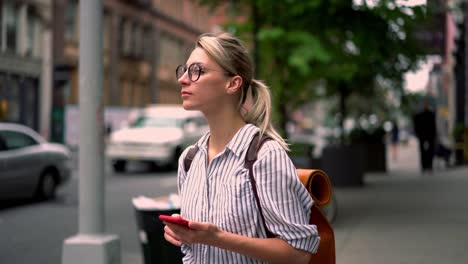 Cheerful-female-tourist-with-rucksack-feeling-carefree-during-trip-for-recreating-sending-sms-message-to-friend-while-walking-on-urban-setting