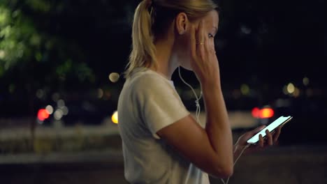 Efecto-a-cámara-lenta-de-la-chica-de-generación-usando-auriculares-electrónicos-para-escuchar-canciones-de-música-durante-la-noche-caminando-por-las-calles-de-la-ciudad