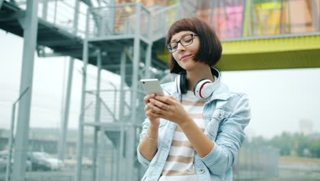 Happy-young-lady-touching-smartphone-screen-standing-outdors-in-city-alone