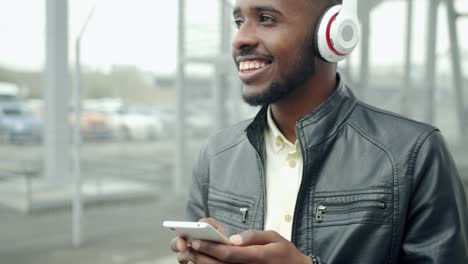 African-American-hipster-in-headphones-touching-smartphone-screen-outside