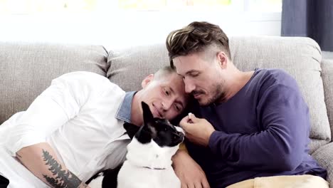 Pareja-gay-relajándose-en-el-sofá-con-perro.-Disfruta-alimentando-a-un-perro.