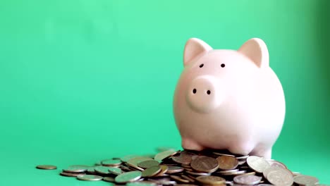 Man-putting-coins-in-piggy-bank-standing-in-pile-of-coins-on-green-background