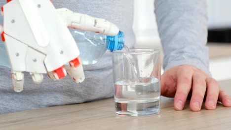 Mann-mit-Roboter-Prothesenhand-gießt-Wasser-in-Glas-aus-der-Flasche-und-trinkt-es-in-der-Küche