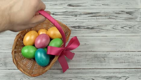 Un-hombre-limpia-una-cesta-de-regalo-con-huevos-de-Pascua-de-colores-de-una-mesa-de-madera,-espacio-de-copia,-decoración