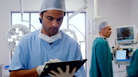 Surgeon-using-digital-tablet-while-colleagues-interacting-in-the-background