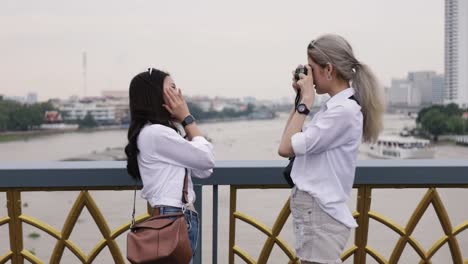 Feliz-pareja-lesbiana-asiática-tomando-una-foto-mientras-está-de-pie-en-el-puente.-Hermosas-mujeres-asiáticas-viajando-con-el-estilo-de-vida-de-vacaciones-de-un-amigo.