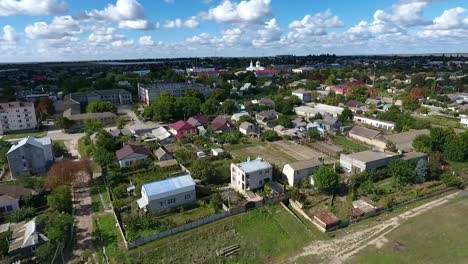 Impresionante-vista-de-pájaro-de-una-periferia-de-la-ciudad-con-cruces-de-caminos,-prados-verdes-y-líneas-de-bloques-de-apartamentos-mezclados-con-pequeñas-casas-en-verano