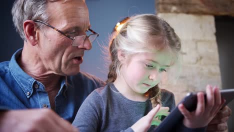 Nahaufnahme-von-Enkelin-mit-Großvater-im-Stuhl-spielen-auf-digitalen-Tablet-zu-Hause-zusammen