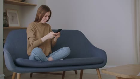 business-woman-typing-message-on-mobile-phone-at-home-office.-Young-girl-chatting-on-phone-in-slow-motion.-Close-up-young-woman-hands-using-smartphone-on-couch.