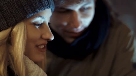 Young-couple-watching-photos-on-smartphone-at-night-in-a-city-street.