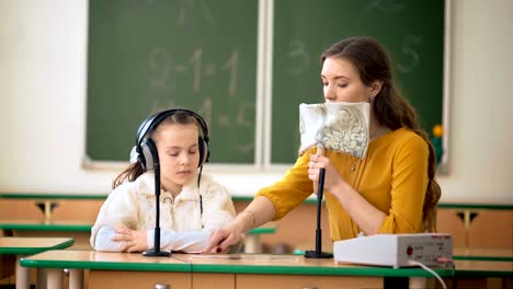 Junges-Mädchen-und-Lehrer-mit-Kopfhörer-und-Mikrofon-im-Klassenzimmer