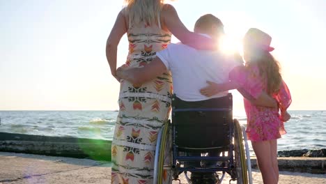 invalid-with-pregnant-woman-and-child-on-background-sea,-husband-in-wheelchair