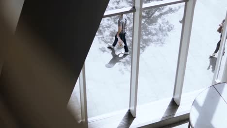 View-inside-the-building.-Young-beautiful-woman-walking-near-the-window-in-office-to-work-in-sunny-day,-using-smartphone