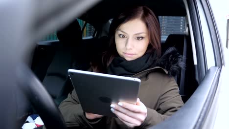 Young-Woman-Typing-Message-on-Tablet-while-Sitting-in-Car