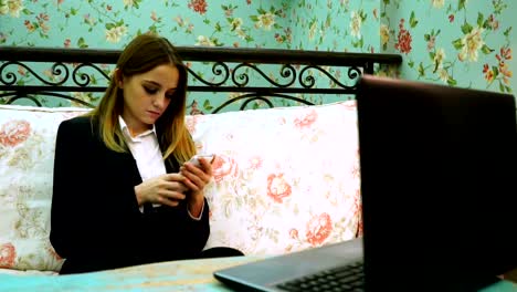 Girl-typing-on-a-smartphone,-in-front-of-a-laptop