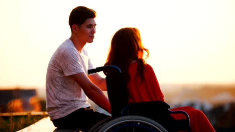 Chica-con-rojo-pelo-es-sentado-en-una-silla-de-ruedas-y-novio-es-sentado-con-ella,-que-hable-acerca-de-algo-y-mira-en-la-distancia