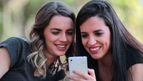 Girlfriends-looking-at-their-cellphones-sharing-social-media-gossip-outdoors