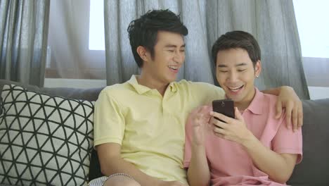 Attractive-young-asian-gay-couple-relaxing-at-home,-talking-and-using-smartphone-together-with-happy-emotion.