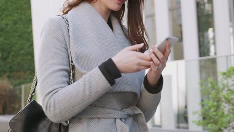 Mid-section-of-young-white-woman-standing-on-a-street-in-London-using-her-smartphone,-close-up