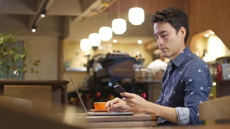 Attraktive-hispanische-junger-Mann-sitzt-allein-in-einem-Café-mit-Laptop-mit-einem-Handy